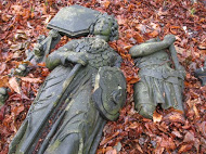A photo of broken figurative stone sculptures laying on the ground surrounded by autumnal leaves